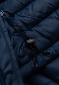 Navy Puffer-Jacke aus Stoff mit gestepptem Design. Verfügt über einen schwarzen Zugregler und einen Kordelzug in der Nähe eines silbernen Reißverschlusses.