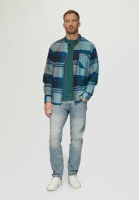 Gestreiftes Baumwollhemd in Blau- und Grüntönen, mit Knopfleiste vorne und Brusttasche. Kombiniert mit hellblauen, verwaschenen Jeans und weißen Sneakers.