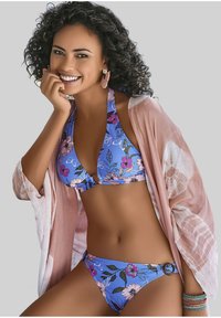 Blauwe bloemenbikini met halternek, voorzien van roze en groene patronen. Vergezeld door een lichtroze doorschijnende cover-up en gestapelde armbanden.