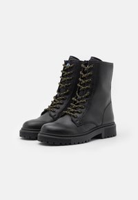 Botas de tobillo de cuero negro con suelas de goma, con cordones acentuados en dorado, punta redonda y un diseño simple y estructurado.