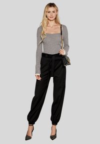 Top grigio a costine a maniche lunghe, pantaloni neri a vita alta con cintura, tacchi a punta neri e una piccola borsa nera con tracolla a catena.