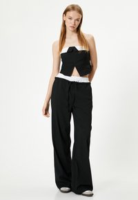 Sort cropped top med hvid kant og sløjfedetalje, parret med sorte breddebukser med elastisk talje og snøre.