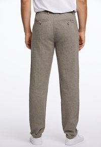 Pantalones de lino color marrón claro con una sutil raya vertical, dos bolsillos traseros con botones y un corte relajado, combinados con zapatos blancos.