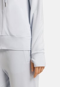 Jasnoniebieska, sportowa bluzka o teksturowanym wykończeniu, z długimi rękawami, przylegającym dołem oraz otworem na kciuk przy mankiecie.