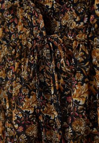 Tissu noir avec des motifs floraux marron, beige et rouge noués en un nœud au centre.