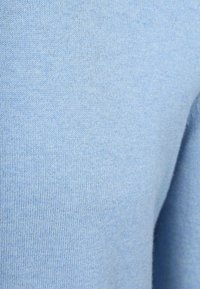 Light blue knitted fabric featuring a smooth texture with fine stitches. The fabric appears soft and even, reflecting subtle variations in color.