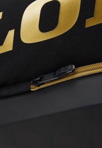 Tessuto nero con lettere dorate, dotato di una cerniera con un cursore nero e una superficie texturizzata di forma rettangolare.