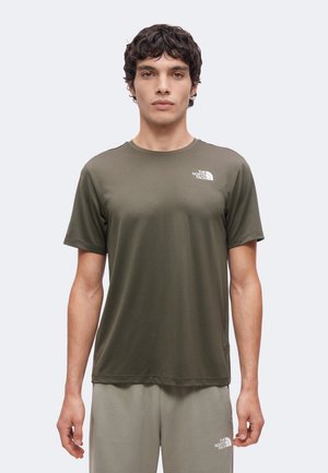 Joven con camiseta de manga corta de The North Face de color verde oliva y pantalones gris claro con logos de la marca en el pecho y el muslo.