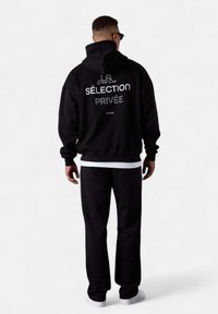 Ensemble sweat à capuche et pantalon noir avec le texte blanc "SÉLECTION PRIVÉE" au dos, avec une coupe décontractée et des poignets et un ourlet côtelés.