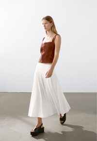 Bordeaux suède cropped top met vierkante halslijn, ritssluiting aan de voorkant, gecombineerd met een vloeiende witte maxi-jurk en zwarte platform sandalen.