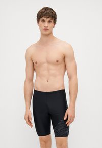 Calções de banho pretos feitos de um tecido elástico, com um padrão geométrico azul de lado. O design é ajustado com uma cintura elástica.