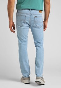 Ljusblå denimjeans med rak skärning, synlig sömnad och bakfickor. Märke på midjebandet. Bärs med ljusa sneakers.