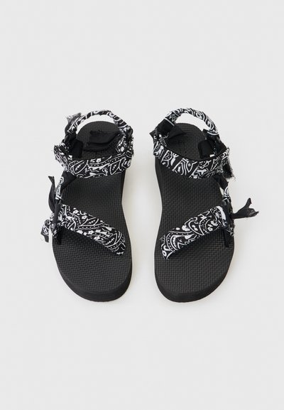 Μαύρα σανδάλια με υφή στη σόλα, με ιμάντες από ύφασμα σε ασπρόμαυρο μοτίβο, που διαθέτουν ρυθμιζόμενα κλεισίματα με βέλκρο και ξεφτισμένες άκρες.