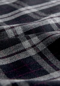 Tissu à carreaux avec des lignes noires, grises et violettes dans une texture douce, présentant un motif tissé et une surface lisse.