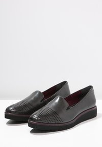Scarpette slip-on in pelle nera con design perforato sulla punta, parte superiore liscia, punta tonda e fodera interna di un rosso scuro a contrasto. Suola in gomma.