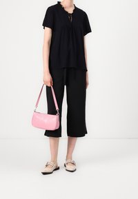 Schwarze, kurzärmelige Bluse mit gerafftem Ausschnitt, kombiniert mit schwarzen, kurzen Hosen und einer kleinen, pinkfarbenen Handtasche mit Krokodilprägung.