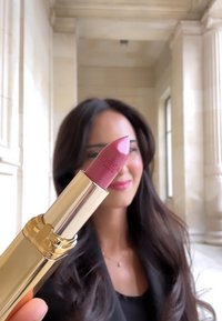 Rosa läppstift i ett guldrör med rundad spets, med ett präglat "L'Oréal Paris"-logotyp. Bakgrunden visar en klassisk inredning med kolonner.