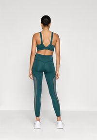 Türkiz sportmelltartó széles pántokkal és V-háttal, hozzá illő, magas derekú leggings, amelyeken hálós panel részletek találhatók az oldalakon.