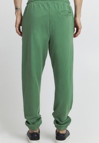 Grønne joggebukser med elastisk talje og mansjetterte anklene. Myk tekstur med et enkelt design. Har en baklomme.