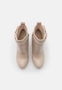 Bottines beige avec motif texturé, bouts pointus, brides latérales avec boucles et languettes à l'arrière, vues de dessus.