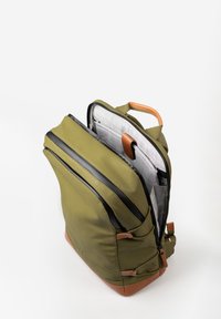Groene rugzak met zwarte ritsen, bruin leren accenten en een textuurinterieur. Bevat meerdere vakken voor organisatie.