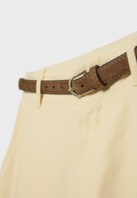 Pantalons couleur crème avec une fine ceinture en daim brun passée dans les passants de ceinture et fixée par une boucle argentée.