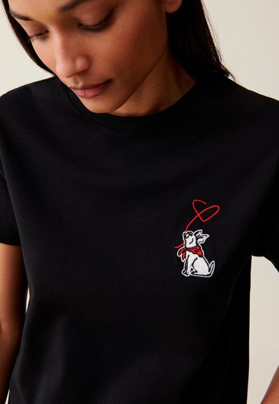 T-shirt en coton noir avec un chien brodé en blanc portant une écharpe rouge et un contour de cœur sur la poitrine, col rond et manches courtes.