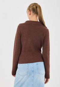 Pull marron à côtes avec col rabattable, silhouette ajustée et manches longues, associé à une jupe en jean bleu clair avec poches arrière.