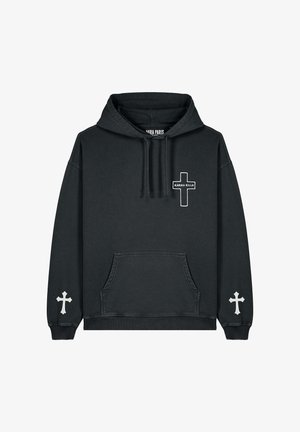 Hoodie noir surdimensionné avec poche frontale, designs de croix blancs sur les manches et la poitrine, associé à un pantalon cargo crème et des baskets blanches.