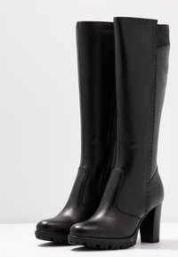 Botas negras de cuero hasta la rodilla con un diseño elegante, punta redondeada, tacón texturizado, paneles laterales elásticos y sutiles acentos perforados.