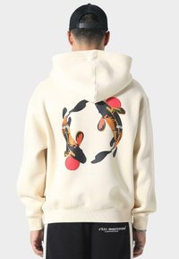 Crème hoodie met een circulair ontwerp van koi-vissen en rode accenten op de achterkant. Zacht materiaal met een relaxte pasvorm en geribbelde zomen.