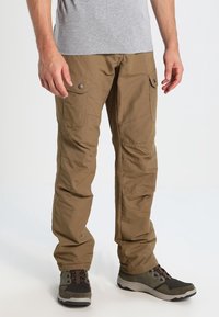 Beige cargo pants with multiple pockets, button accents, straight leg design, and a smooth texture, worn with gray shoes and a gray shirt.