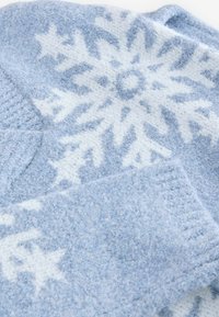 Ljusblå tröja med vit snöflinge mönster. Mjuk, texturerad tyg och ribbade ärmslut. Överklippta sektioner visar varierande nyanser.