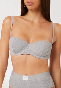Grijze geribbelde bralette met beugel, verstelbare bandjes en een merklabel aan de onderkant. Glad textuur en aansluitend ontwerp.