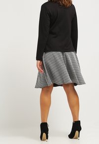 Czarny top z długim rękawem połączony z rozszerzaną spódnicą w czarno-białe kropki. Modelka nosi czarne botki na wysokim obcasie.