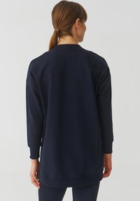 Marineblauwe oversized sweatshirt met lange mouwen, geribbelde halslijn en manchetten, met een soepele textuur en zijsplitten aan de zoom.