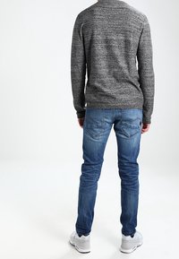 Grå stickad tröja med långa ärmar, kombinerad med blå jeans med en urblekt effekt, och vita sneakers. Vy från baksidan.