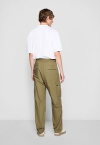 Olivgrüne Cargo-Hosen mit elastischem Bund und mehreren Seitentaschen, kombiniert mit einem schlichten weißen T-Shirt mit kurzen Ärmeln.