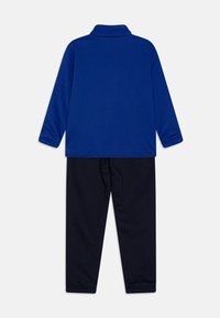 Camisa polo de manga larga azul con cuello combinada con pantalones de chándal negros. Ambos artículos tienen una textura suave y un corte relajado.