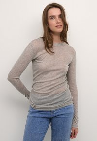 Svetlo siva majica z dolgimi rokavi iz mehkega, prosojnega pletenega materiala, prilegajoče oblike in okroglim izrezom, združena z modrimi jeans hlačami.