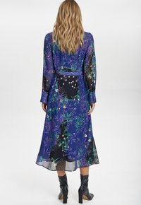 Langarm, mid-lange jurk van doorzichtige paarse stof met bloemen- en geometrische patronen, strak cinched bij de taille met een bijpassende riem.