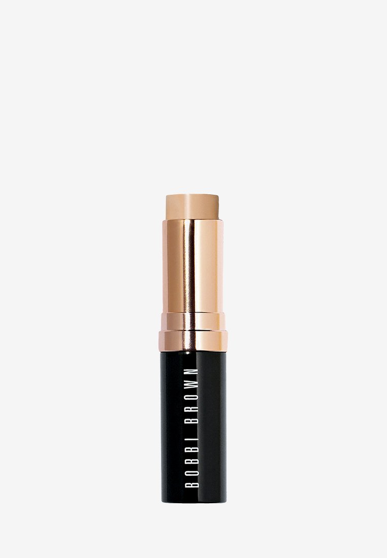 Fond de teint en stick Bobbi Brown dans un tube cylindrique noir avec un capuchon doré brillant. La surface noire texturée affiche le logo de la marque en lettres blanches.