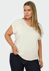 T-shirt beige clair à manches courtes avec un col en V, fabriqué en tissu doux. Associé à un jean bleu foncé. Présente une coupe décontractée et une texture lisse.