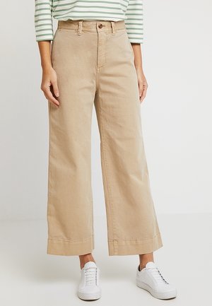 Hellbeige, weit geschnittene Hosen aus Baumwolle mit hoher Taille, vorderen Taschen und umgeschlagenen Säumen, kombiniert mit weißen Turnschuhen und einem gestreiften Oberteil.