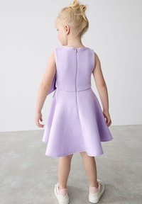 Lila brezrokavna obleka z embosiranim vzorcem 'B', razpetim krilom, zadrgo na hrbtu in v kombinaciji z svetlo roza supergami. Gladka tekstura.