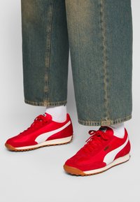 Red athletic shoes with white accents, featuring a combination of smooth and textured materials, round toe, and contrasting rubber sole.