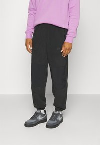 Joggers neri con pannelli in tessuto a contrasto, tasca con zip e logo Nike discreto. Abbinati a sneakers grigio scuro e a una felpa viola.
