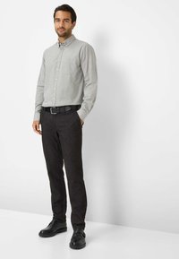 Graues Hemd mit Knöpfen und einer Tasche, kombiniert mit dunklen Hosen und schwarzen Schuhen. Glatter Stoff, taillierte Passform und klassisches Design.