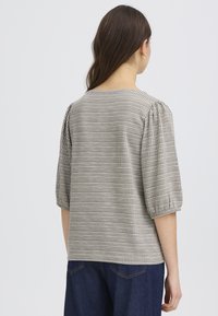 Blouse à carreaux gris et blancs avec des manches bouffantes, un col rond et un tissu texturé. Portée avec un jean denim foncé.