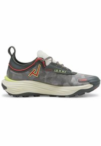 Chaussure de sport grise avec un motif camouflage, tige en tissu texturé, accents rouges et verts, et une épaisse semelle blanche. Dotée d'une languette et de lacets.